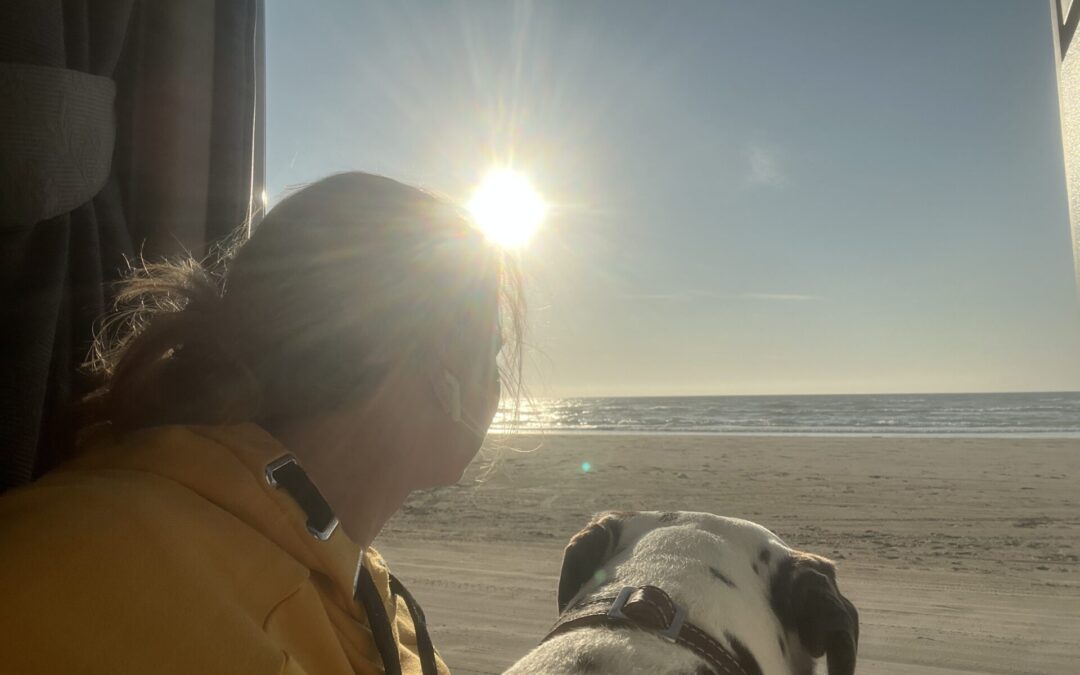 Sarah Both und Alma sitzen in der Seitentür ihres Campers und schauen aufs Meer und der untergehenden Sonne entgegen