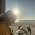 Sarah Both und Alma sitzen in der Seitentür ihres Campers und schauen aufs Meer und der untergehenden Sonne entgegen